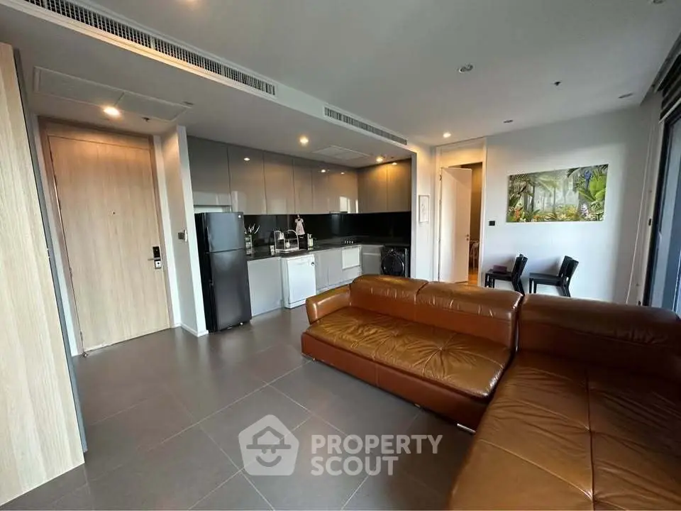 Modern living room with brown leather sofa and sleek kitchen in open layout apartment.