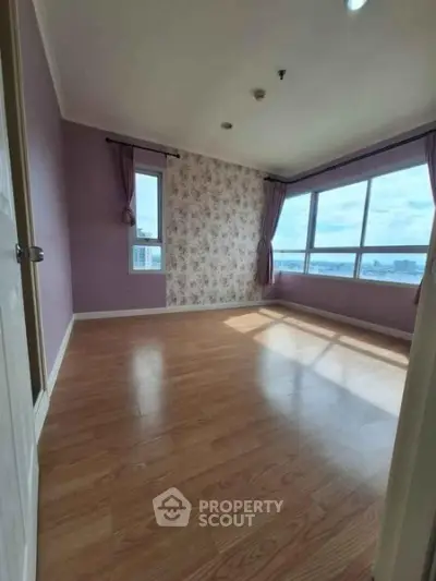 Spacious empty bedroom with large windows and wooden flooring, offering ample natural light and city views.