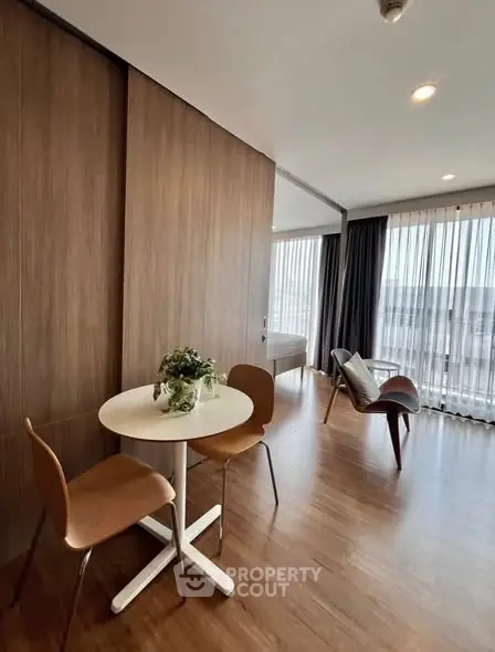 Modern living room with wooden flooring, stylish furniture, and large windows offering natural light.