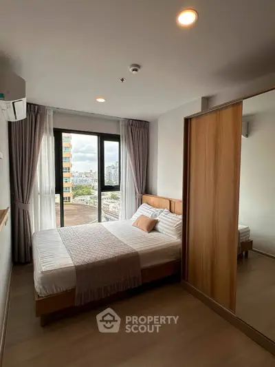 Modern bedroom with city view, featuring a cozy bed and large window for natural light.