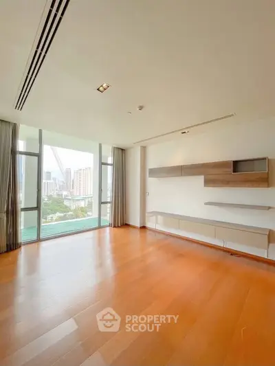 Spacious modern living room with large windows and city view, featuring sleek built-in shelves and wooden flooring.