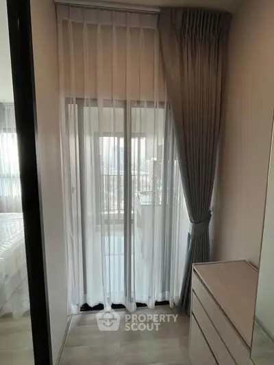 Cozy bedroom with sheer curtains and modern dresser, offering a glimpse of a bright balcony.