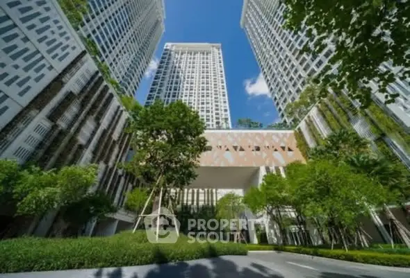 Stunning modern high-rise building with lush green landscaping and clear blue sky.