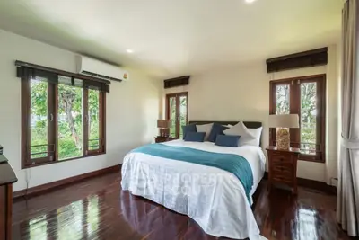 Spacious bedroom with large windows and elegant wooden flooring, offering a serene garden view.