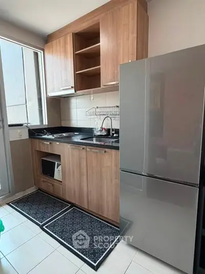 Modern kitchen with sleek wooden cabinets and stainless steel fridge in a compact layout.