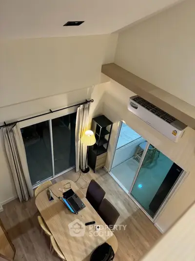 Modern living room with high ceiling and large windows, featuring a cozy dining area and air conditioning.