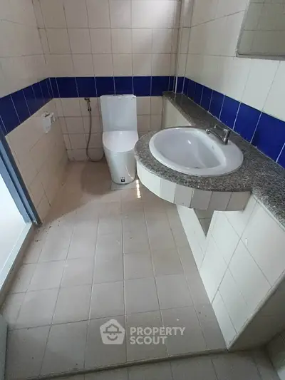 Modern bathroom with sleek sink and toilet, featuring blue accent tiles and spacious layout.