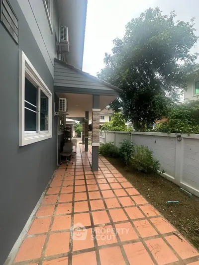 Charming side pathway of modern home with tiled flooring and lush greenery.