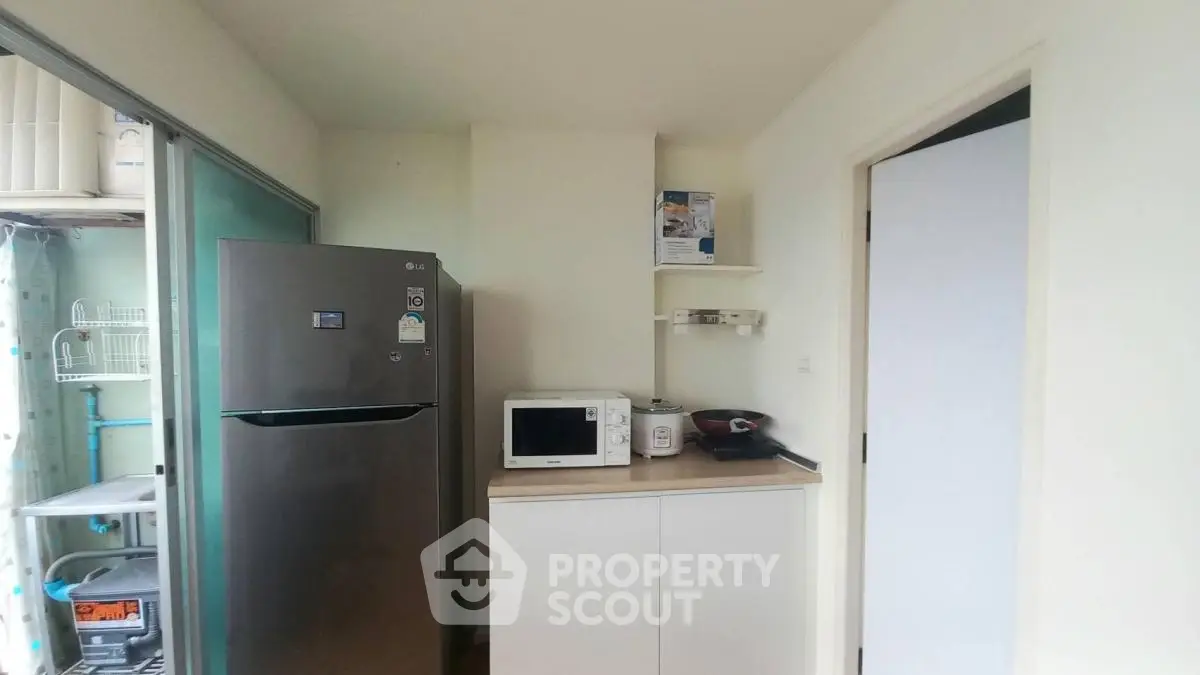 Compact kitchen with fridge, microwave, and storage cabinets in modern apartment.