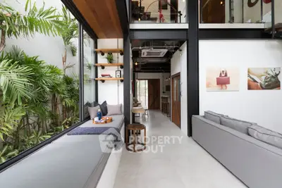 Modern living room with large windows and lush indoor plants, featuring stylish decor and open layout.
