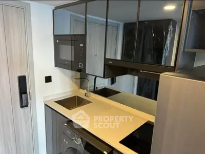 Modern compact kitchen with sleek appliances and mirrored cabinets in a stylish apartment.