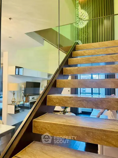 Luxurious modern staircase with glass railing in a stylish living room, featuring elegant decor and natural light.