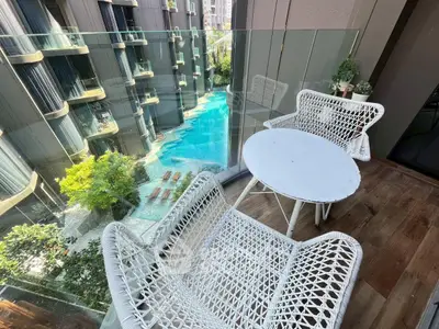 Stylish balcony with wicker furniture overlooking a luxurious pool in a modern apartment complex.