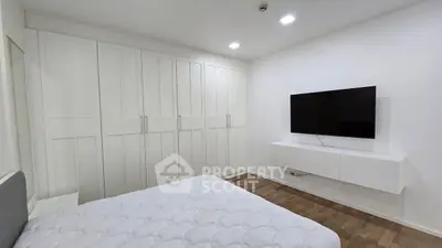 Spacious bedroom with modern wardrobe and wall-mounted TV, featuring sleek design and ample storage.