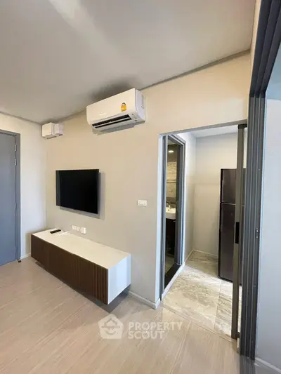Modern living room with wall-mounted TV and air conditioning, leading to a sleek kitchen area.