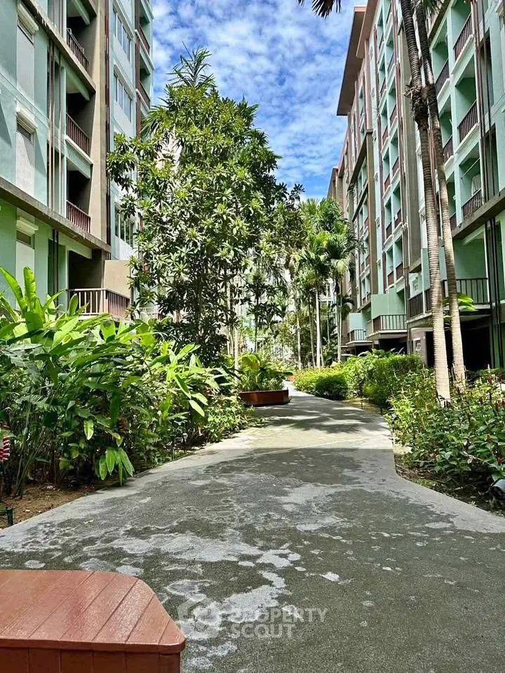 Lush garden pathway in modern residential complex with tall buildings and tropical plants.