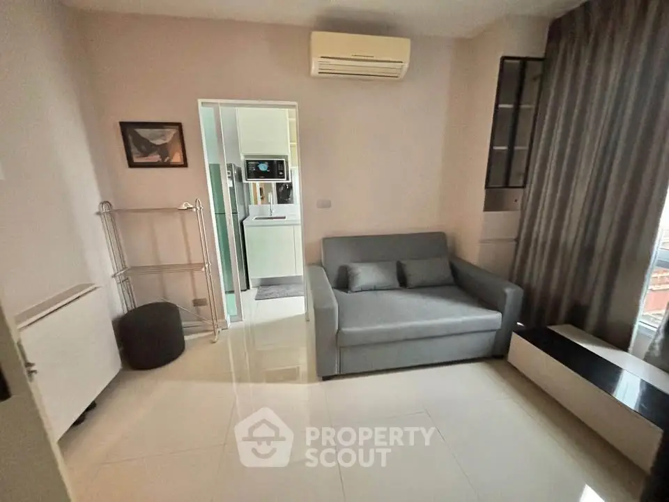 Modern living room with sleek sofa and air conditioning, adjacent to a compact kitchen area.