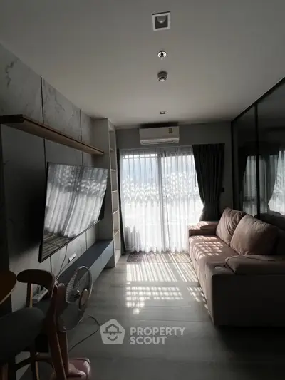 Modern living room with large TV, cozy sofa, and natural light from window.