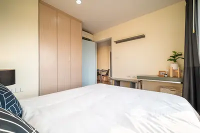 Spacious bedroom with large bed, built-in wooden wardrobe, and a sleek study area complemented by natural light.