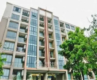 Modern multi-story residential building with glass facade and lush greenery.