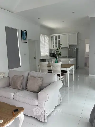 Charming open-plan living room and kitchen with elegant white decor and cozy seating area.