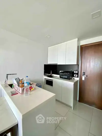 Modern compact kitchen with sleek white cabinetry and black accents, featuring a microwave and minimalist design.