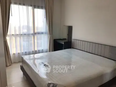 Spacious bedroom with large window and modern furnishings in a high-rise apartment.