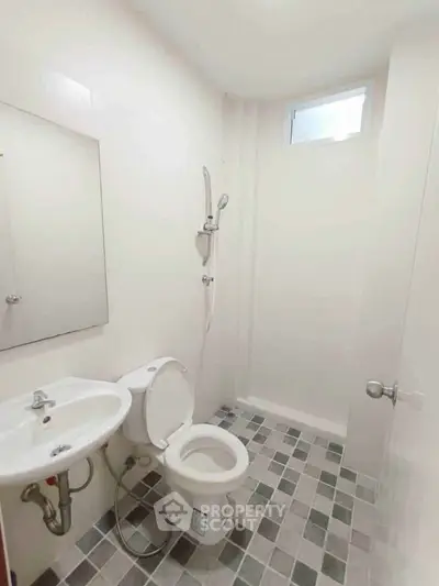 Compact bathroom with modern fixtures and tiled floor, featuring a shower and small window for natural light.