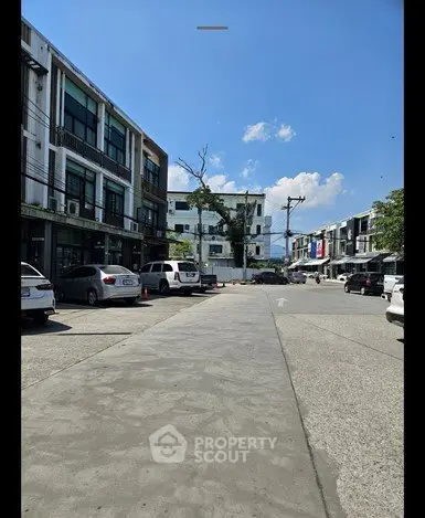 Modern urban street view with commercial buildings and parked cars under a clear blue sky.
