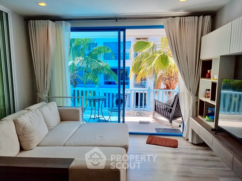Spacious and inviting living room with plush sofa and direct access to a sunlit balcony with tropical palm views, perfect for relaxation and entertaining guests.