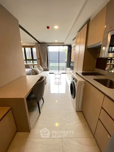Modern open-plan living room with sleek kitchen and washing machine, bright and spacious design.