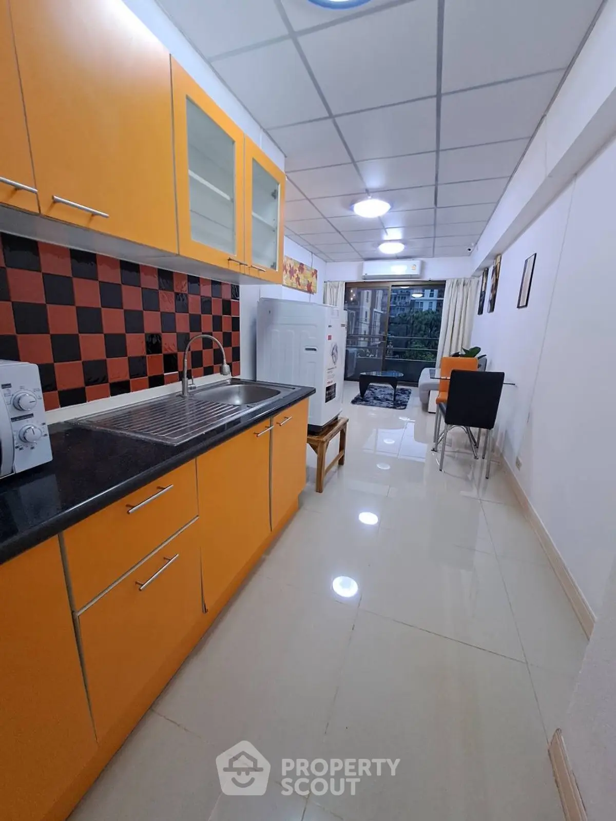 Modern kitchen with vibrant orange cabinets and dining area in a sleek apartment.