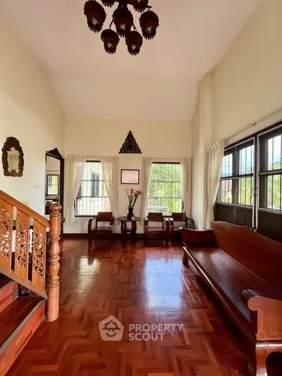 Elegant living room with wooden flooring and classic furniture, featuring large windows and decorative lighting.
