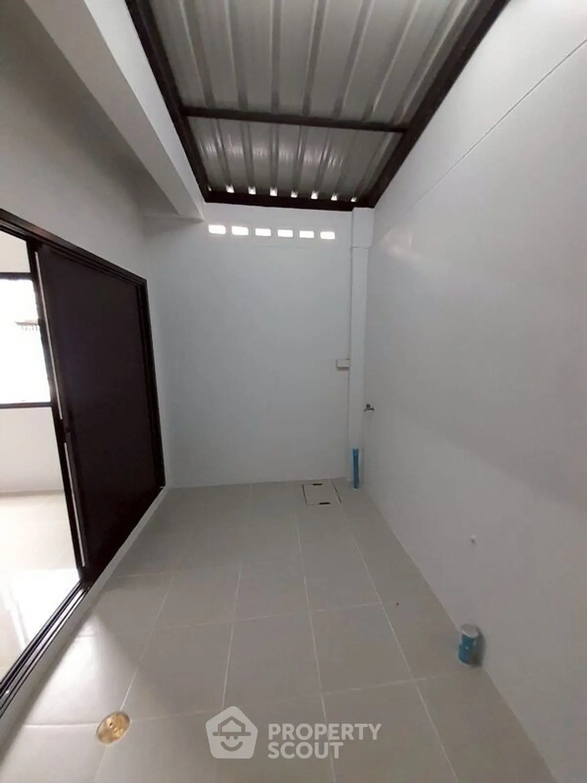 Spacious tiled area with sliding glass door and metal roof, ideal for utility or storage.