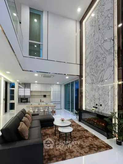 Luxurious modern living room with high ceilings, marble accent wall, and open kitchen layout.
