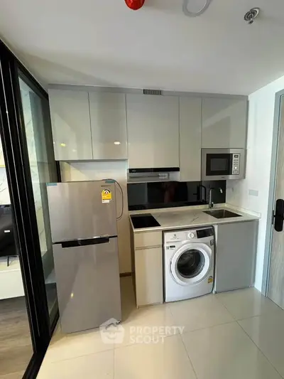 Modern compact kitchen with sleek appliances and washing machine in a stylish apartment.