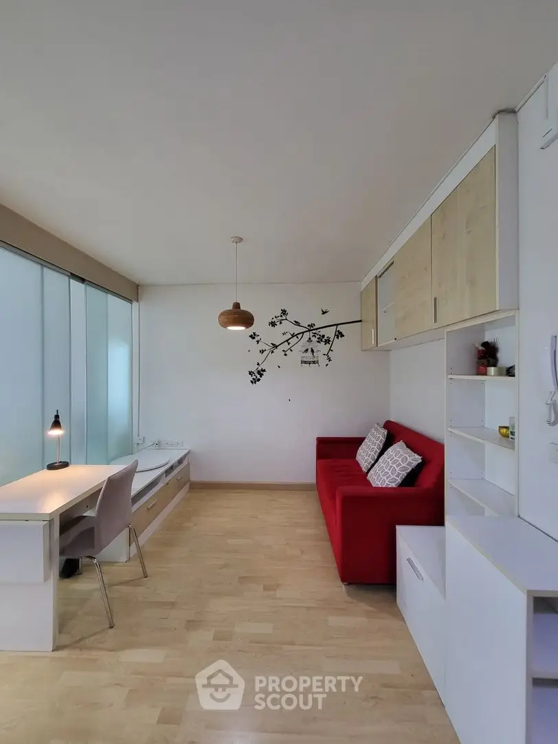 Modern living room with red sofa, built-in storage, and natural light from large windows.