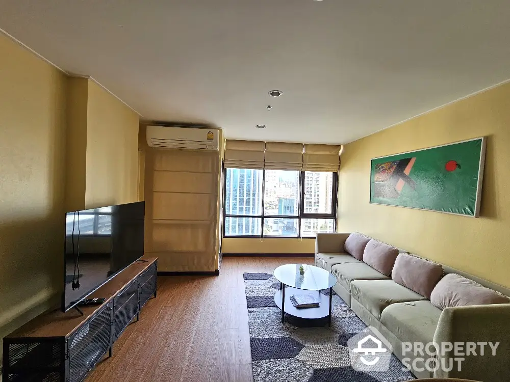 Spacious living room with modern decor and city view, featuring a large TV and comfortable sofa.