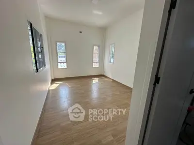 Spacious empty room with wooden flooring and ample natural light from multiple windows.