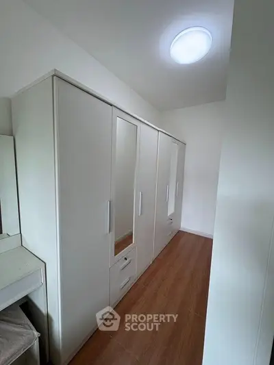 Spacious walk-in closet with sleek white cabinetry and wooden flooring