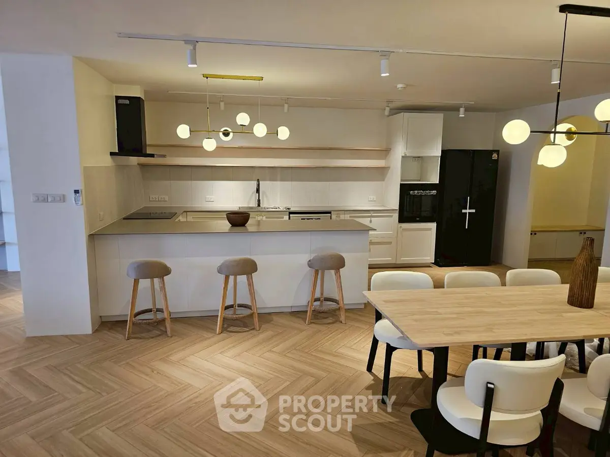 Modern open kitchen with dining area, featuring sleek appliances and stylish lighting.