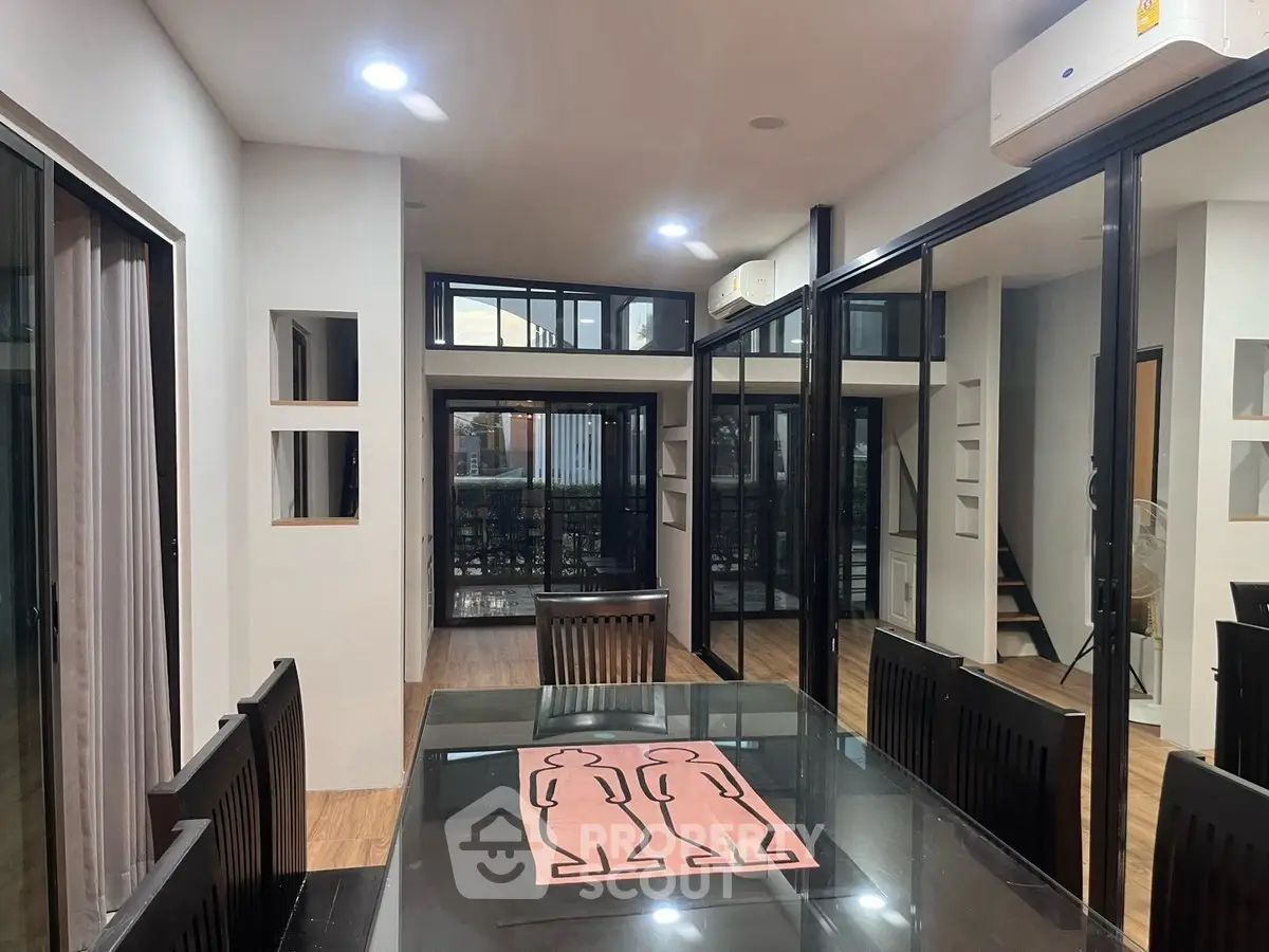 Modern dining area with glass table and air conditioning, featuring sleek design and ample natural light.