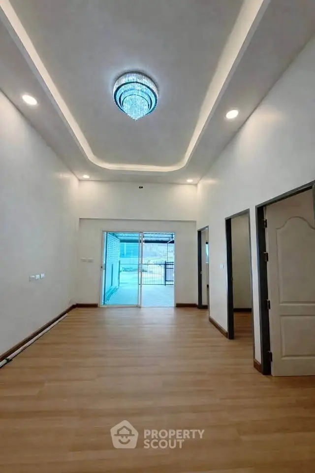Spacious living room with elegant chandelier and wooden flooring, leading to a bright outdoor area.