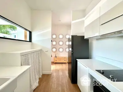 Modern kitchen with sleek white cabinets and black appliances, featuring unique circular window design.