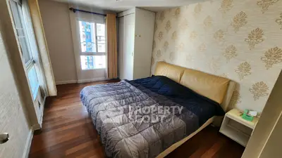 Cozy bedroom with elegant wallpaper and wooden flooring, featuring a comfortable bed and natural light.