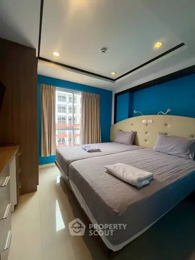 Modern bedroom with twin beds and vibrant blue accent wall in urban apartment.