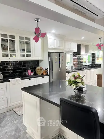 Spacious modern kitchen with sleek black countertops and white cabinetry, featuring stainless steel appliances and elegant decor.