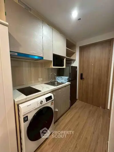 Modern compact kitchen with washing machine and wooden cabinetry in cozy apartment.