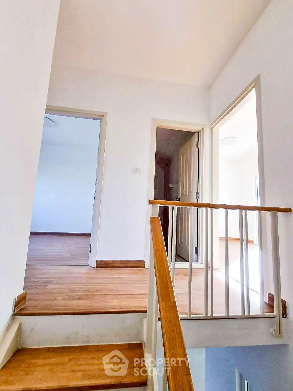 Bright and airy hallway with wooden flooring and white walls, leading to multiple rooms in a modern home.