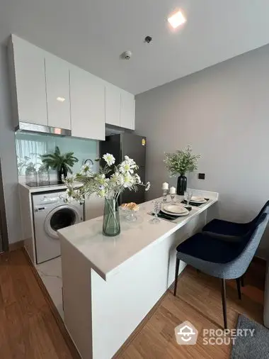 Modern kitchen with open layout featuring sleek white cabinetry, integrated appliances, and a cozy dining area with stylish decor.